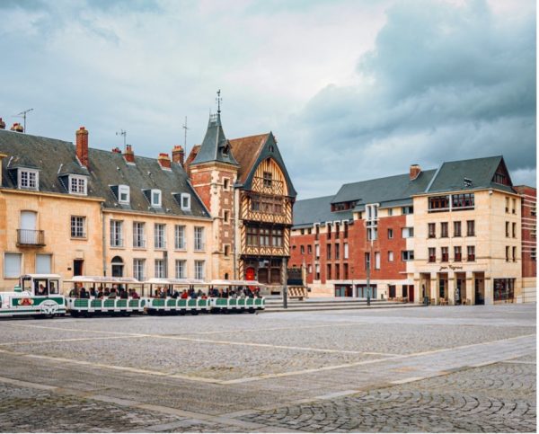 Place de l’Hôtel de Ville d’Amiens avec ses bâtiments anciens et le petit train touristique sous un ciel nuageux