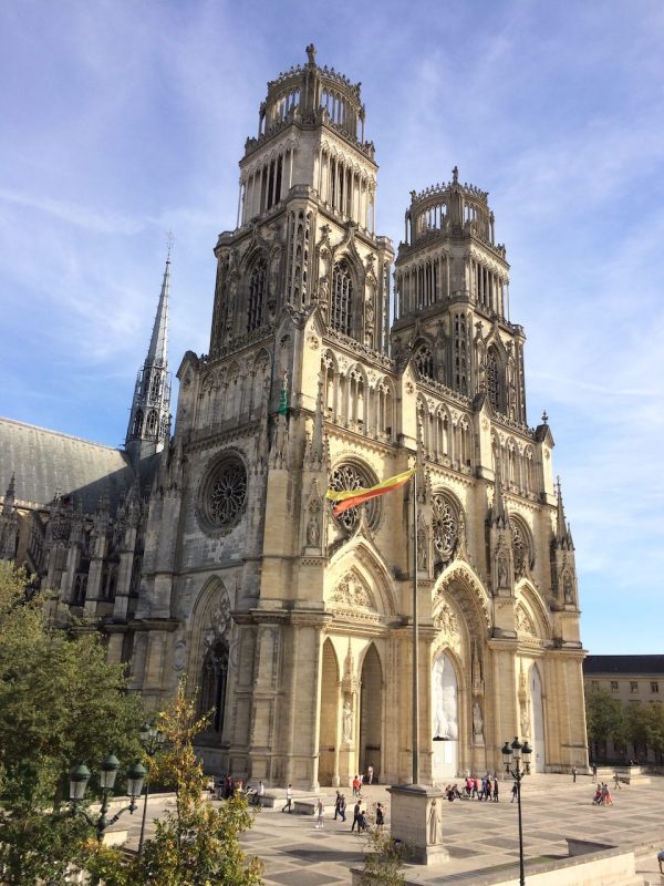 Vue de la cathédrale Sainte-Croix d’Orléans avec ses deux tours gothiques sous un ciel bleu, et des visiteurs sur la place