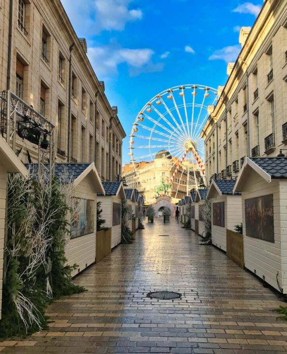 Allée du marché de Noël d’Orléans bordée de chalets en bois avec une grande roue illuminée en arrière-plan