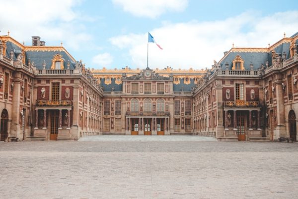Cour d’honneur du Château de Versailles avec façade dorée et drapeau français flottant au-dessus du palais