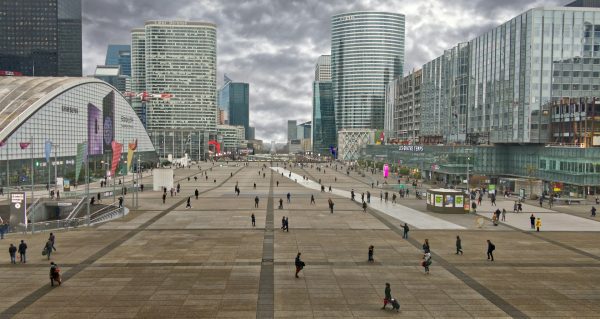 Vue de l’esplanade de La Défense avec gratte-ciel, passants et bâtiments modernes sous un ciel nuageux