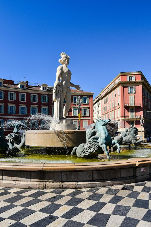 Fontaine du Soleil sur la Place Masséna à Nice avec la statue d’Apollon et les bâtiments rouges emblématiques sous un ciel bleu