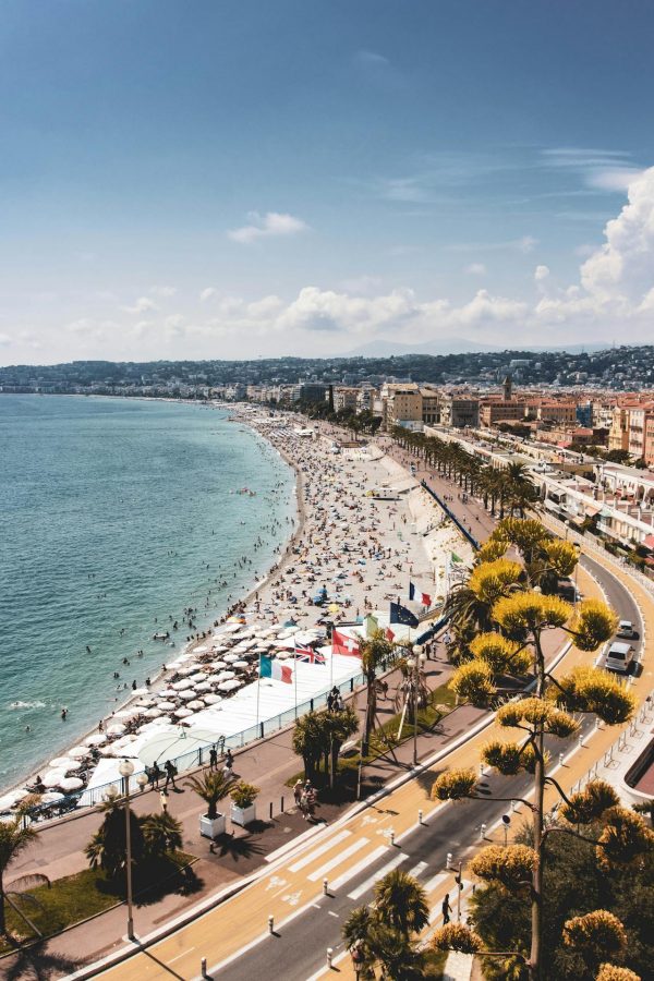 Vue aérienne de la Promenade des Anglais à Nice avec plage bondée, mer turquoise et immeubles en bord de mer sous un ciel bleu