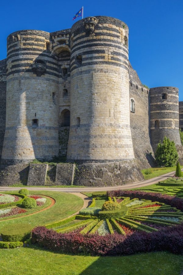 Tours monumentales du château d’Angers avec ses remparts et jardins au premier plan sous un ciel bleu