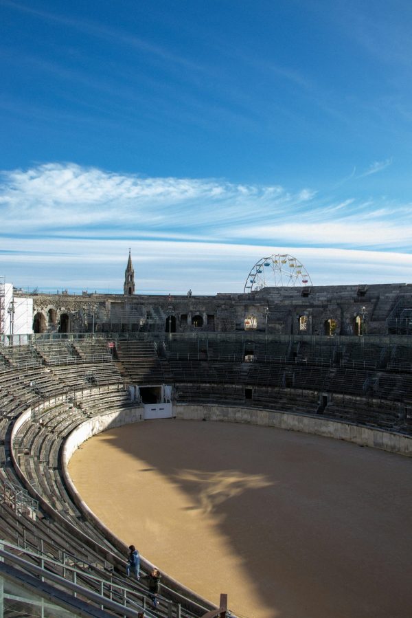 Vue intérieure des Arènes de Nîmes, amphithéâtre romain avec gradins en pierre et piste centrale sous un ciel bleu