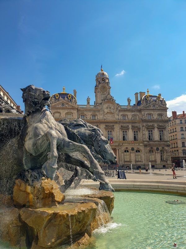 Fontaine Bartholdi sur la place des Terreaux à Lyon, sculpture monumentale avec chevaux et bassin, devant l’Hôtel de Ville sous un ciel dégagé
